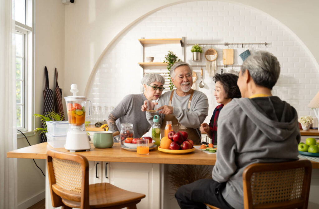 A group of older adults standing around a kitchen island that's filled with fruits, vegetables, and a blender, making fruit-infused water and smoothies