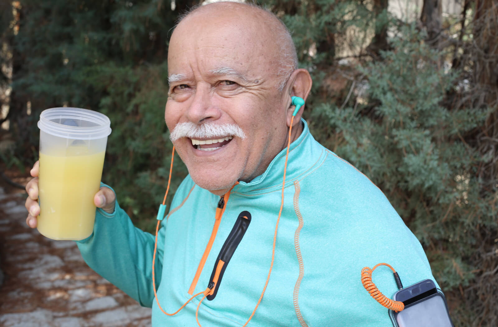 An older adult man with earphones in, holding a protein shake while getting some exercise