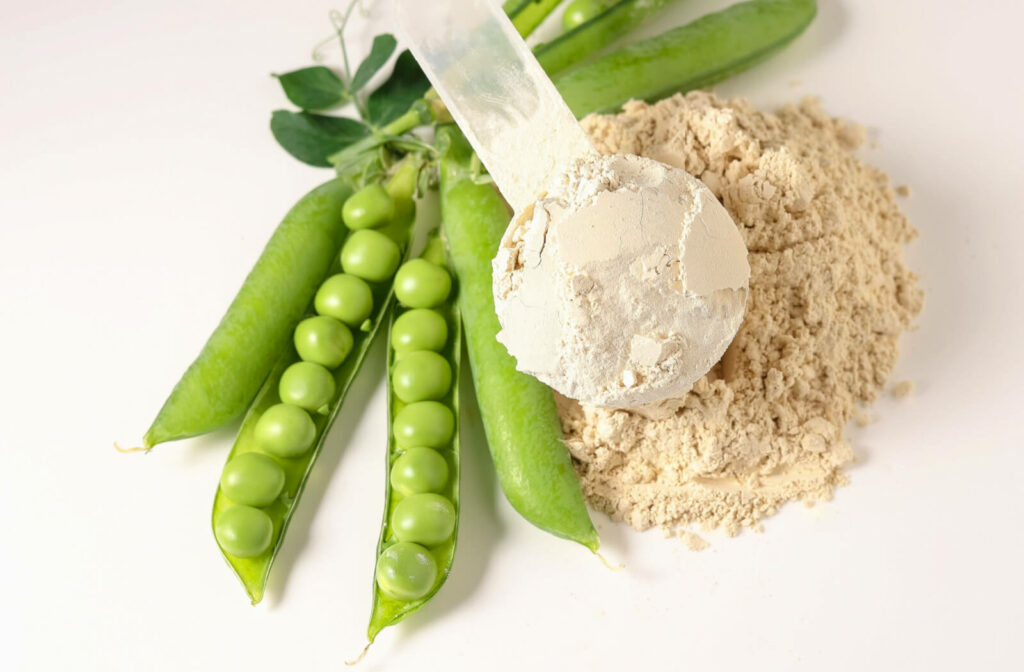 Close-up of a plant based pea protein powder in plastic scoop with fresh green peas seeds on white background