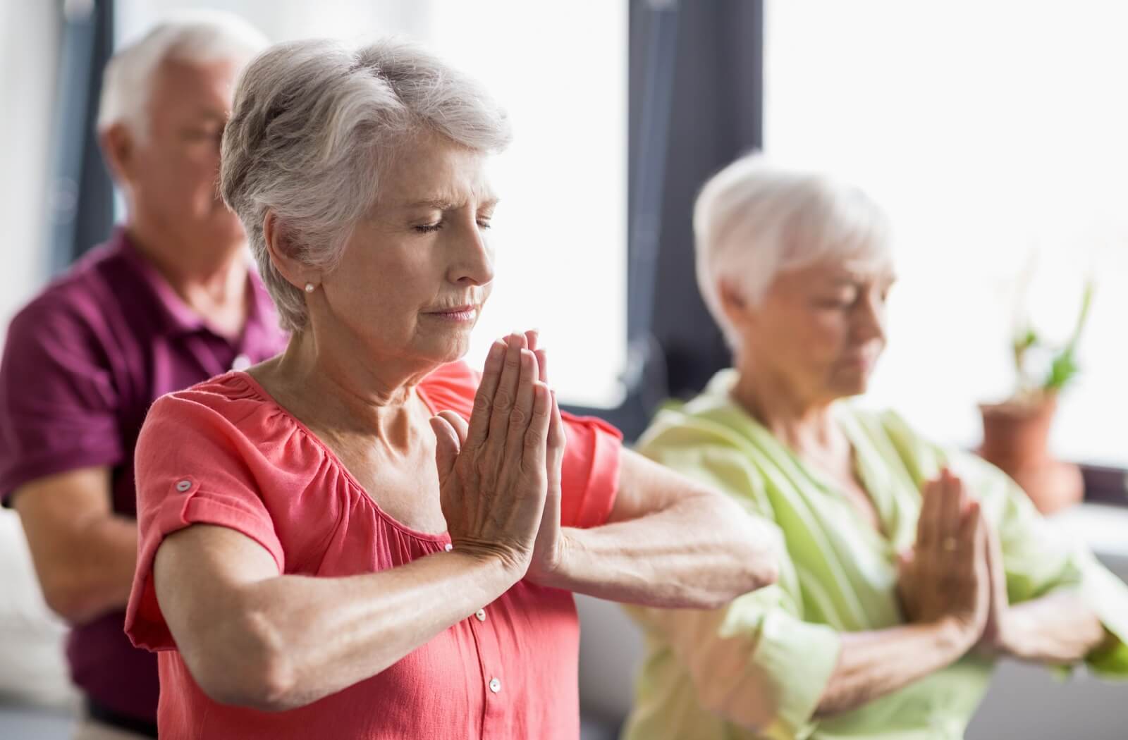 A group of seniors with closed eyes practicing yoga and sitting on yoga mats