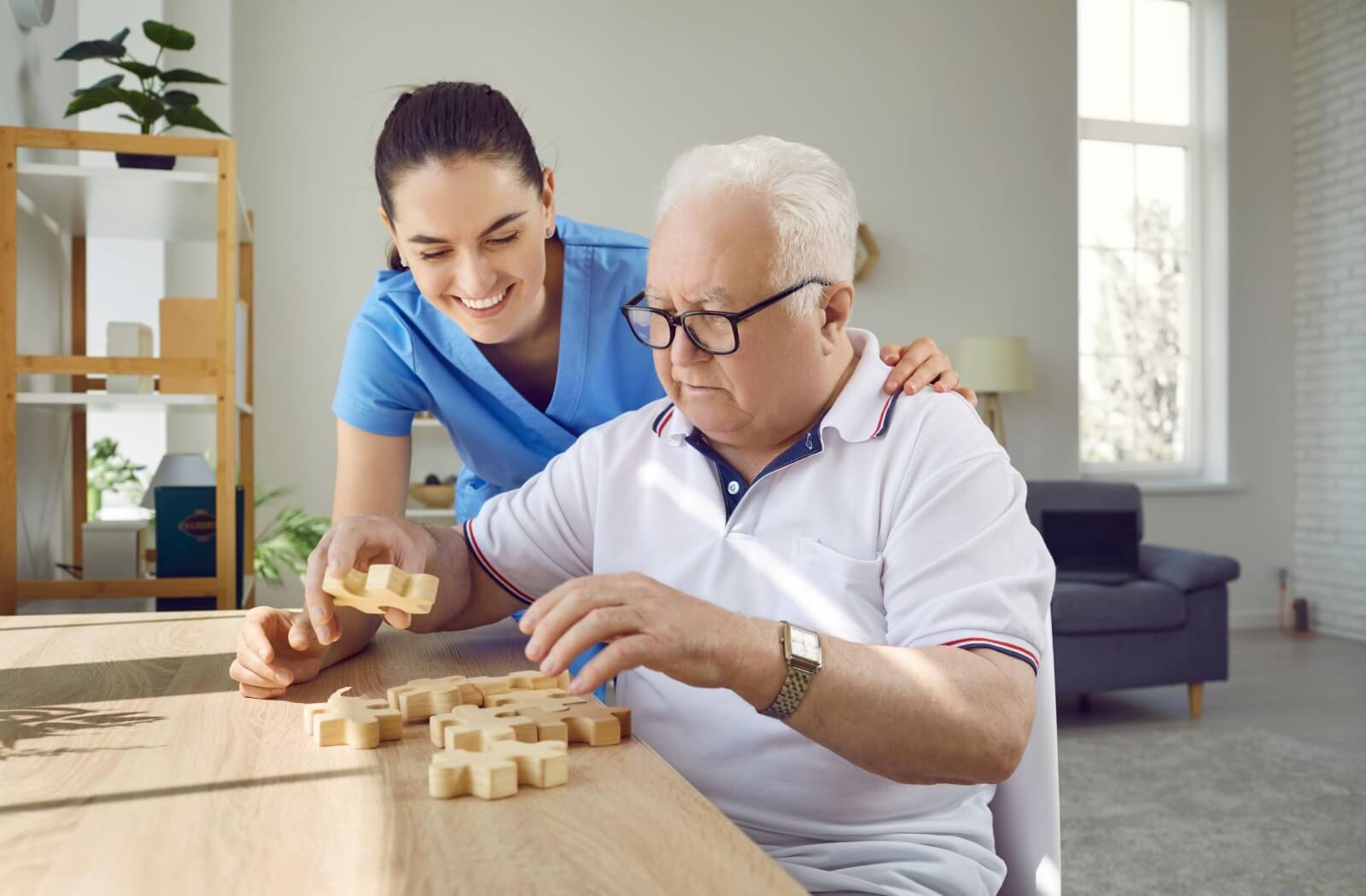 A memory care staff member helping an older adult solve a wooden jigsaw puzzle.