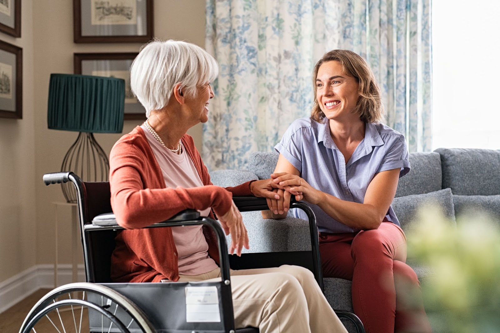 A smiling woman holding the hand of a senior woman with Parkinson's.