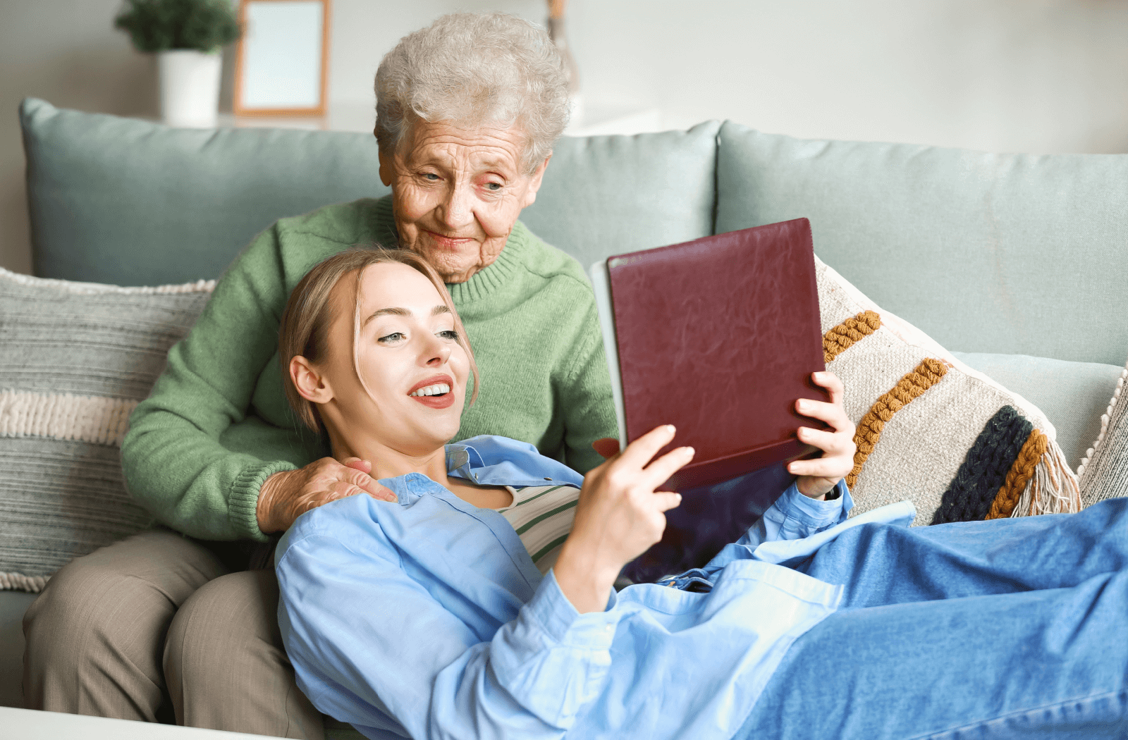 A young adult lays in their grandparent's lap on the couch as they flip through a photo album together