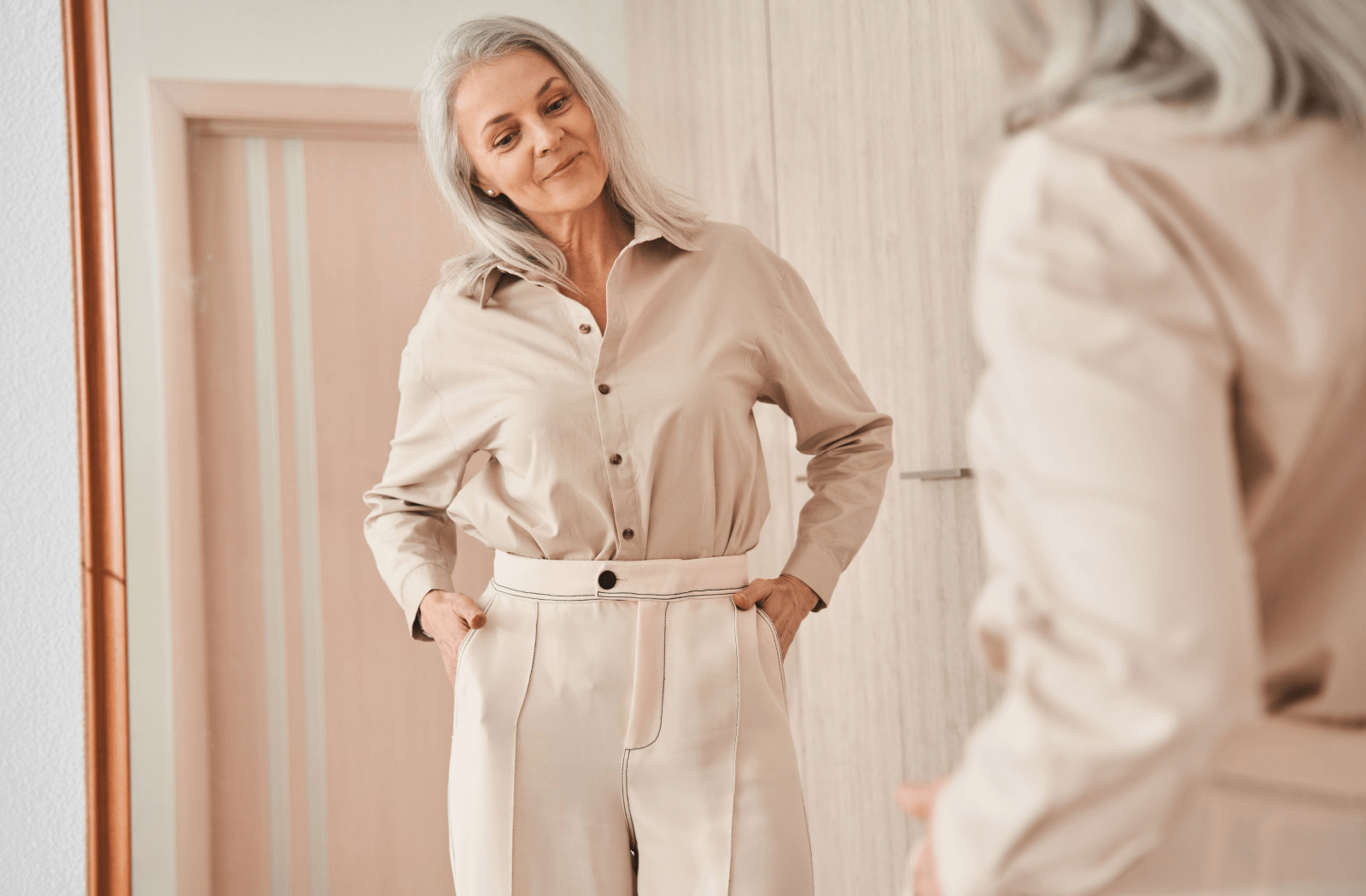 A senior dressed in white slacks admires their outfit in the mirror.